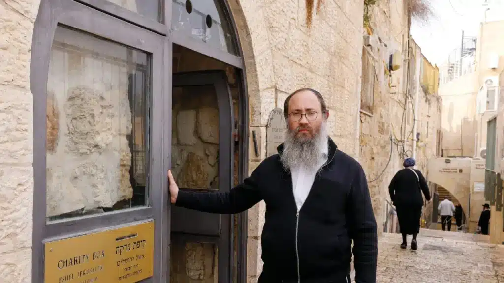 Un homme se tient à l'entrée d'un centre de bienfaisance dans la vieille ville de Jérusalem, avec une plaque indiquant "Charity Box - Eshel Jerusalem".