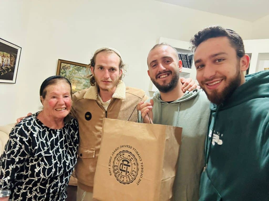 Groupe de jeunes hommes et une femme plus âgée se tenant par le bras et tenant un sac en papier brun Colel Chabad.