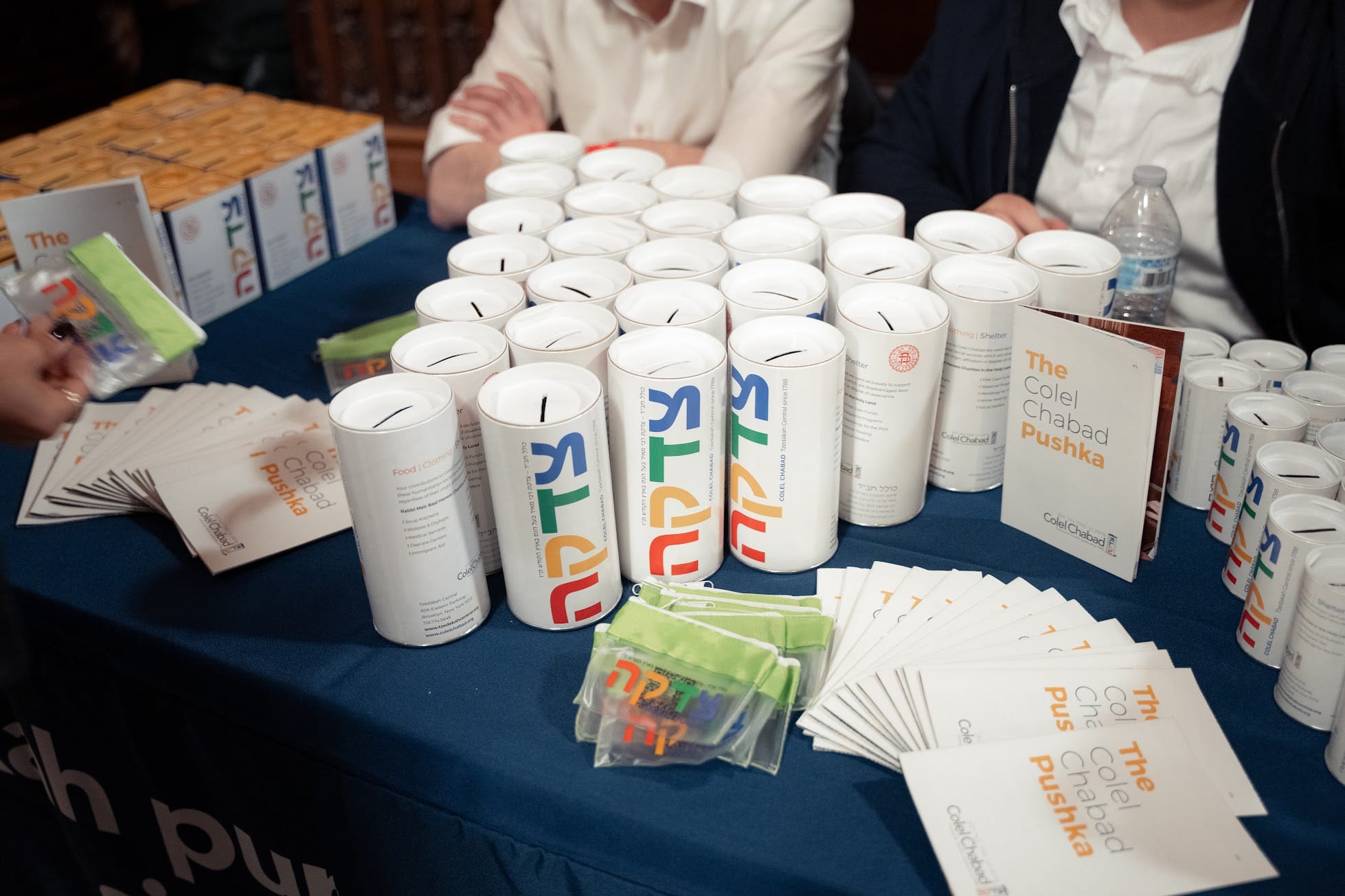 Une table avec des récipients pour les dons, des dépliants sur lesquels on peut lire ‘the colel chabad pushka’.’