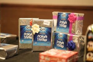 Wrapped Hanukkah gifts in silver paper with Hebrew written on the front, stacked on a table.